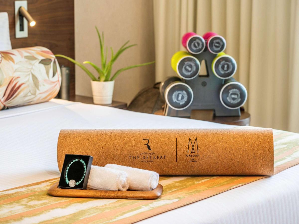 The Retreat Palm Dubai Mgallery By Sofitel Zewnętrze zdjęcie The photo shows a well-decorated hotel room with a neatly made bed. On the bed, there is a cylindrical cork container with a logo, indicating a brand or establishment. Next to it, there are two rolled-up towels resting on a small wooden tray. In the 